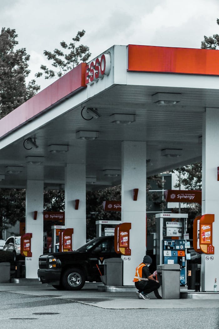 Gas station with a person refueling a car under a bright canopy, surrounded by trees.